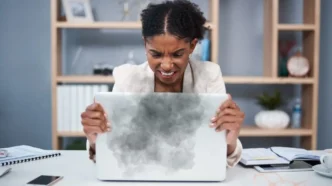 Frustrated user holding a laptop showing signs of overheating like warning icons and fan noise
