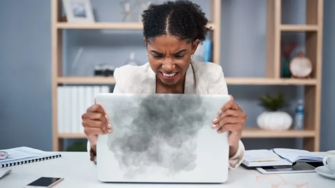 Frustrated user holding a laptop showing signs of overheating like warning icons and fan noise